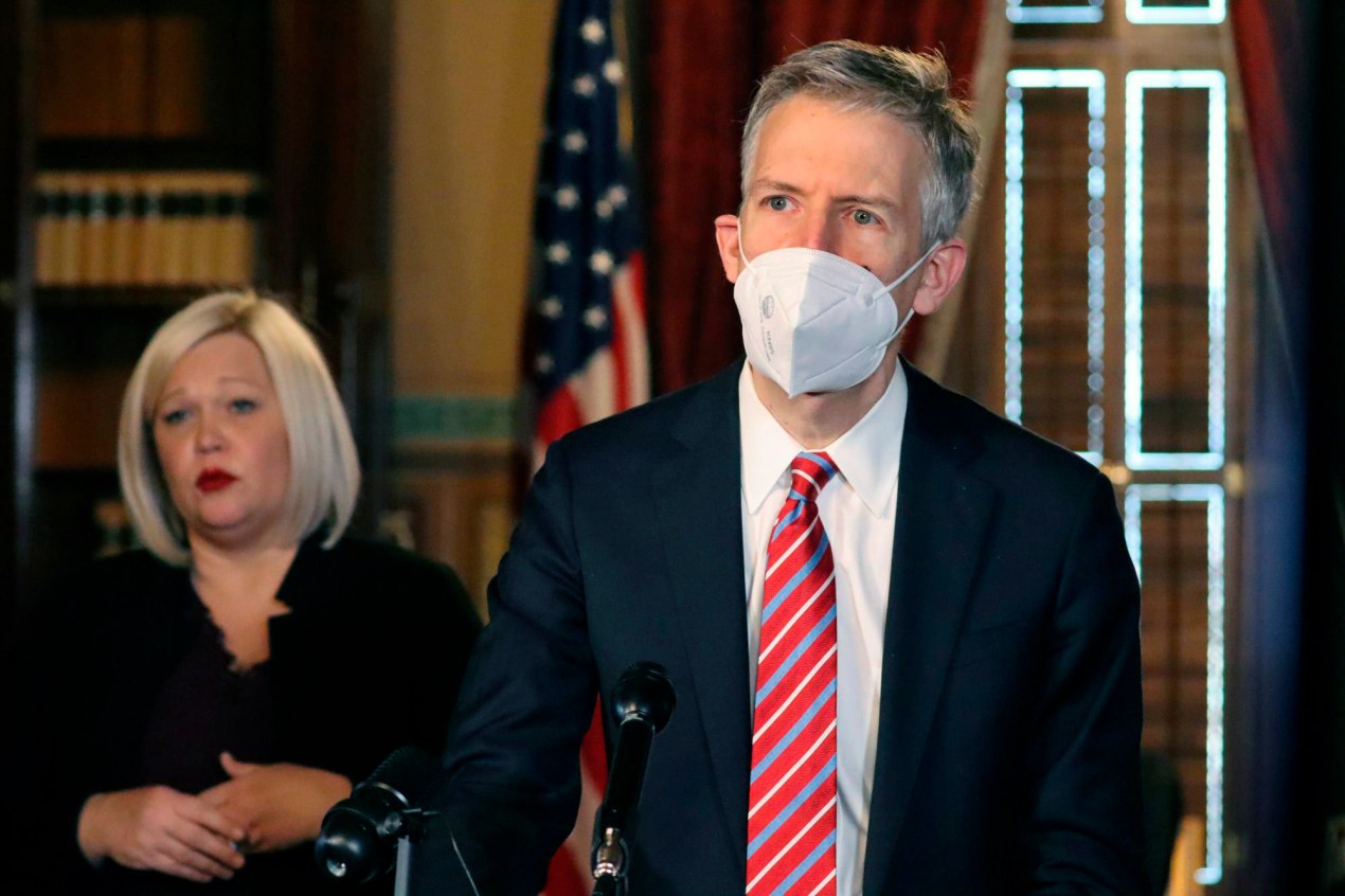 A photo of a man in a suit wearing a KN-95 mask at an official event.