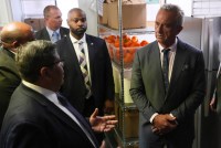 A photo of Robert F. Kennedy Jr. receiving a tour of a food distribution center. Shelves behind him show crates filled with orange bell peppers.