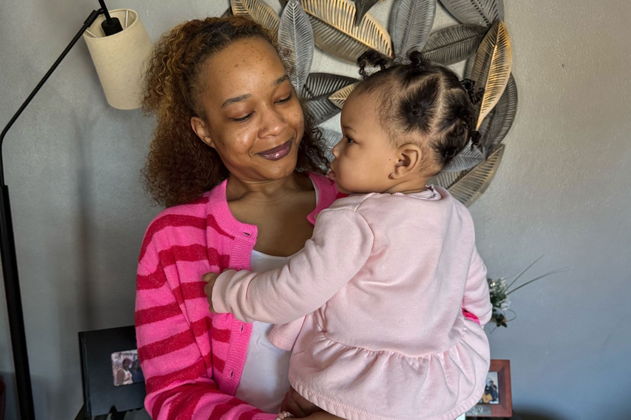 A Black woman holds her young daughter in her arms. She is smiling at her daughter.
