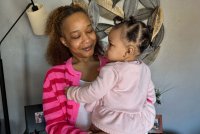 A Black woman holds her young daughter in her arms. She is smiling at her daughter.