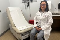 A photo of a doctor sitting by an exam chair in her office.