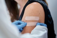 A close-cropped shot of a doctor wearing blue gloves giving second adhesive bandage to a young woman after administering vaccines.