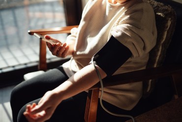 A photo of a woman sitting in a chair from the shoulders down. She is taking her blood pressure.