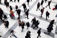 A photo of a train station as commuters and pedestrians walk hurriedly around the frame. Their forms are blurred as they are in motion.