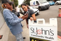 A woman is showing another woman something on a cell phone screen. In front of them is a sign that reads, "St. John's Community Health."