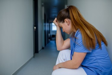 An exhausted health care worker crouches down to rest, exhibiting exhaustion.