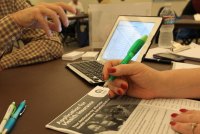 A photo of a laptop on a table. In the foreground is a woman holding a pen over a Covered California information packet.