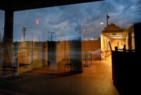 A photo of a dimly lit hospital entrance seen through a window. The window is reflecting a view of the parking lot behind the photographer.