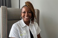 A portrait of a woman smiling at the camera and wearing a white blouse with a name tag.