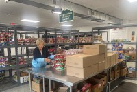 A woman standing before a metal table sorts boxes of non-perishable foods