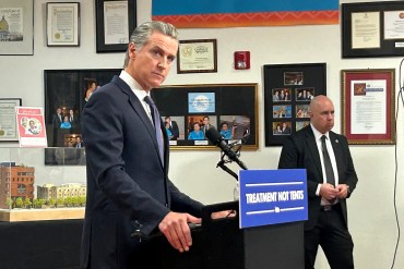 Gavin Newsom speaks at a news conference behind a podium with a sign on it that reads, "Treatment not tents."