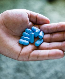 A hand holds nine light blue pills.