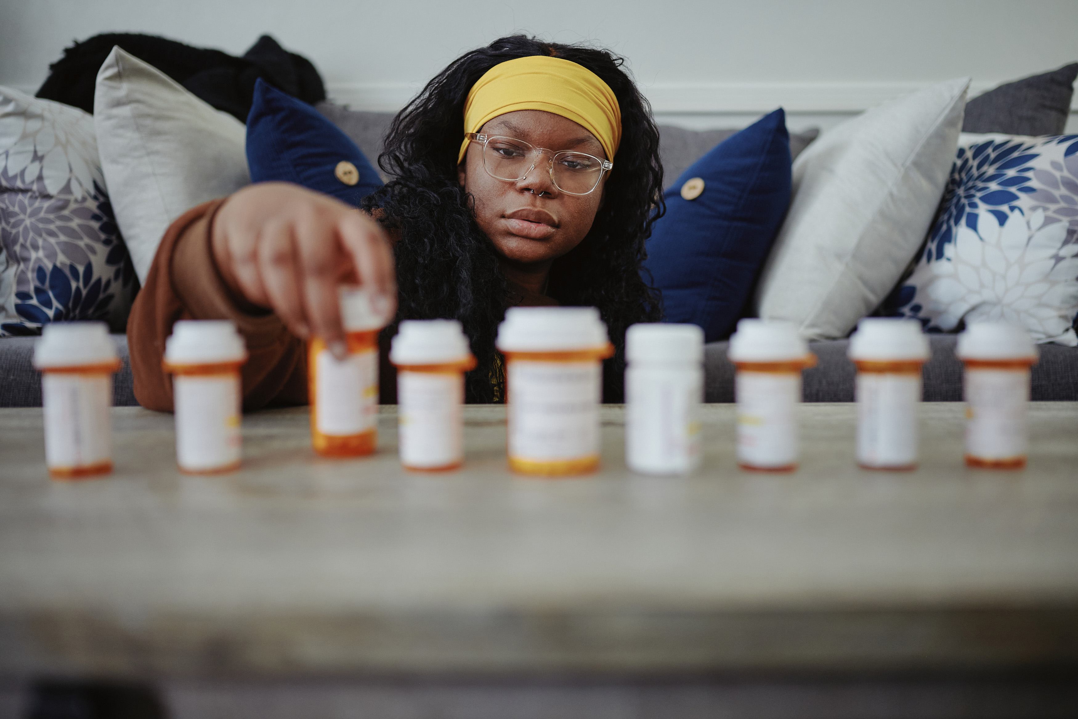 A woman with dark hair wearing a yellow headband looks at prescription bottles lined up on a table
