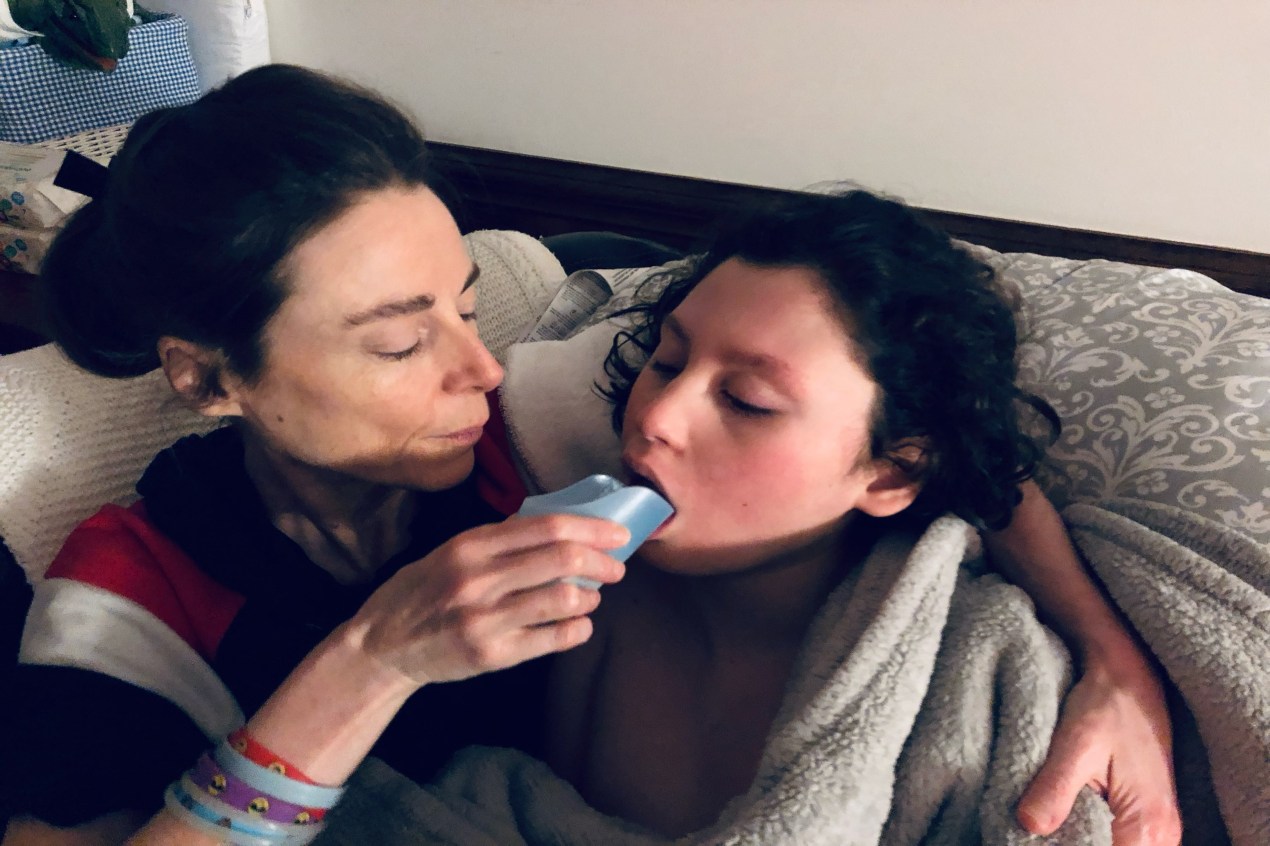 A woman embraces a young boy, feeding him a liquid from a small cup