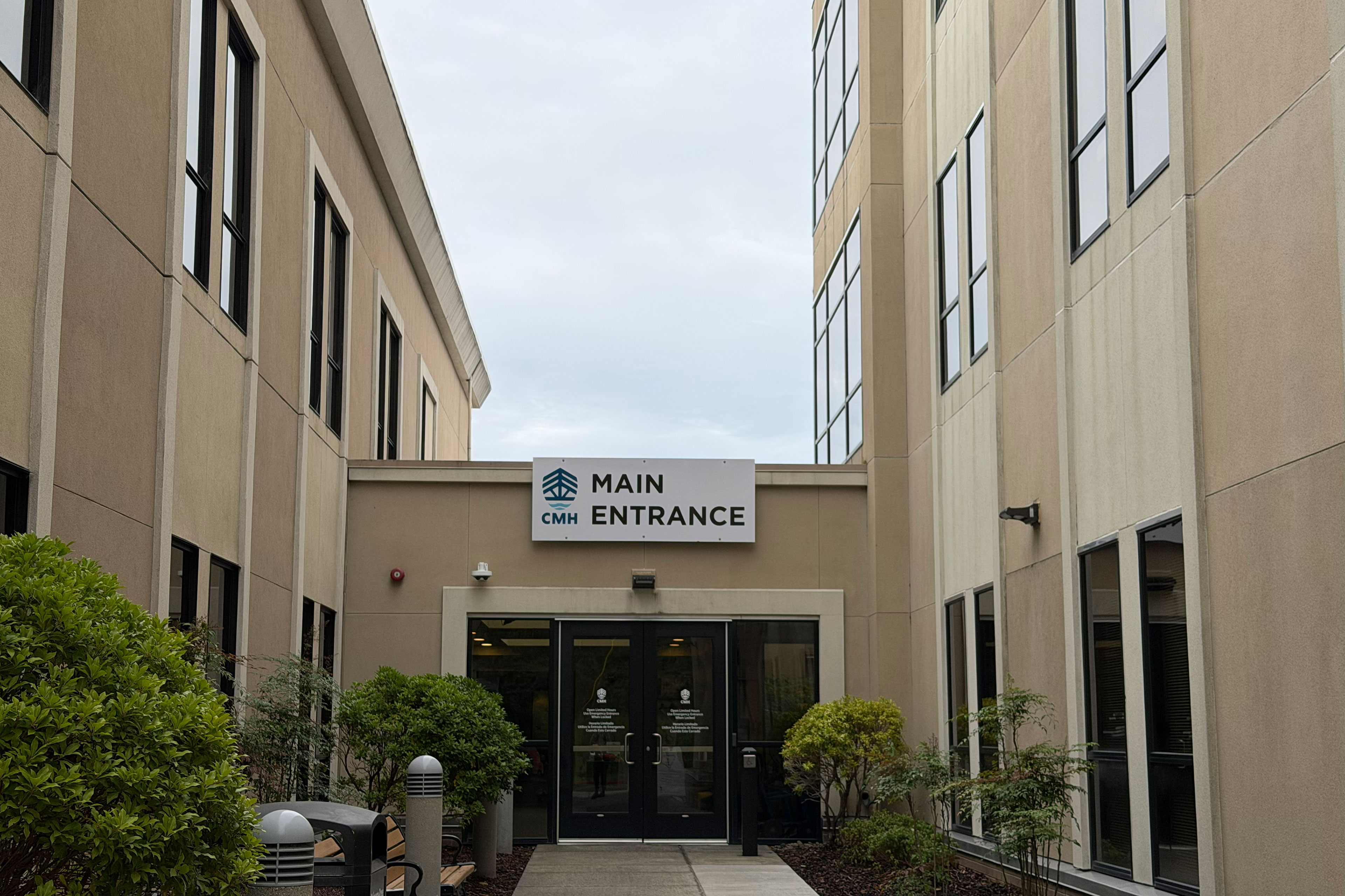 A sign reading "Main Entrance" is positioned above doors in a single-story section of a building. Taller parts of the building are attached on either side.