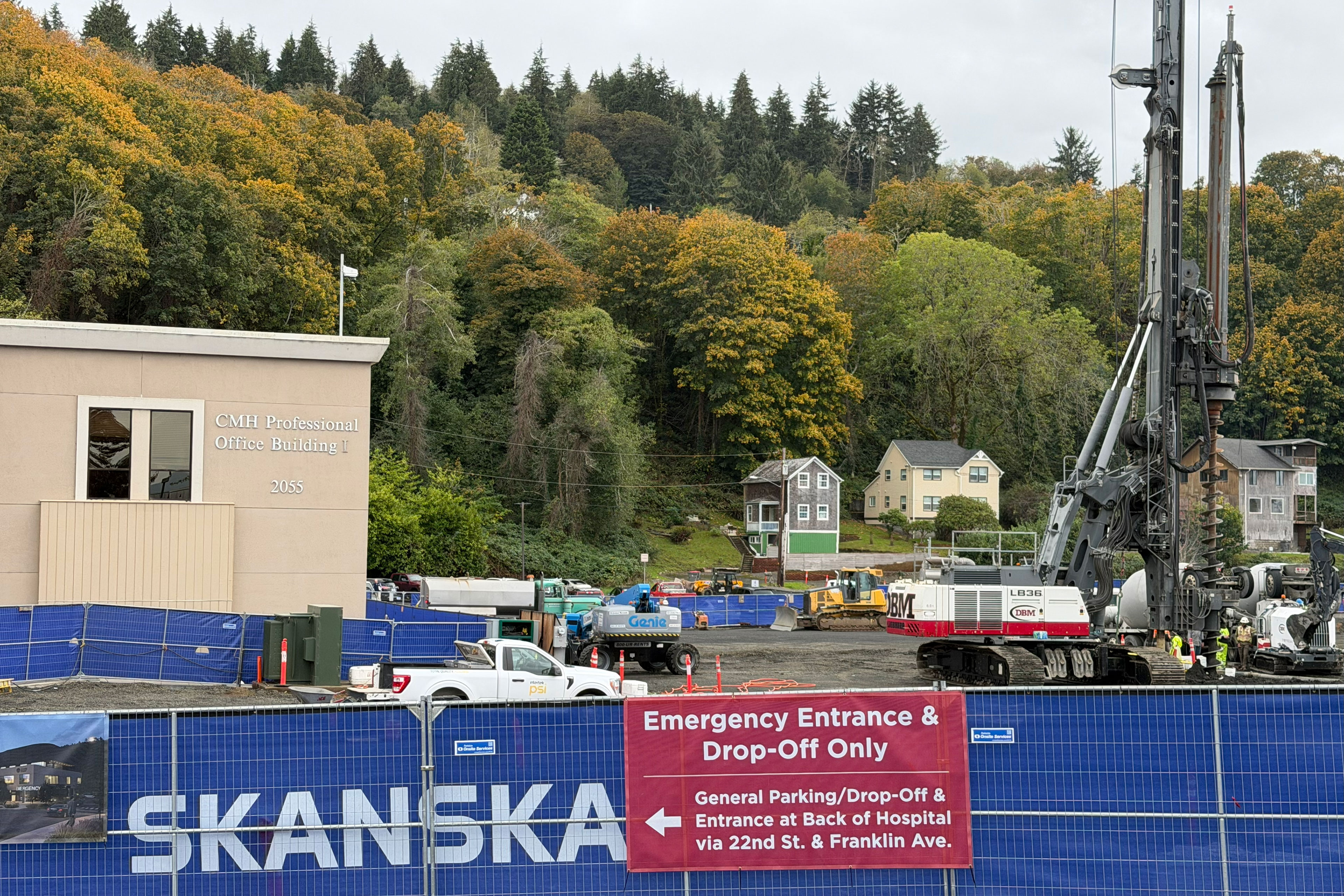 A construction site is next to a low building with "CMH Professional Office Building I 2055" lettering on it. Fencing in front of the construction has a red sign with white lettering that reads "Emergency Entrance & Drop-Off Only" and a arrow point left with additional wording about additional parking.