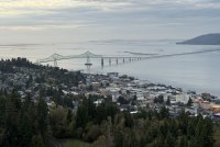 The view from a nearby hill of a city at the edge of a river and a bridge spanning that river.