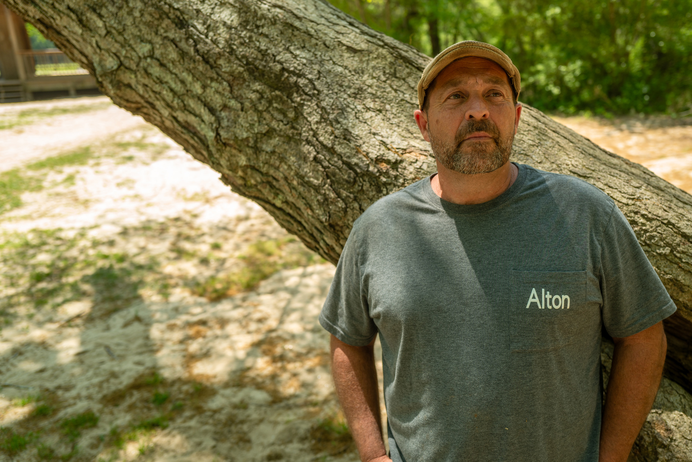 A portrait of a man outdoors, leaning his back against a tree trunk.
