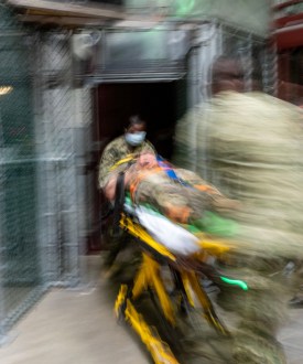 A photo with motion blur showing a gurney being pushed by medics in camo uniforms.