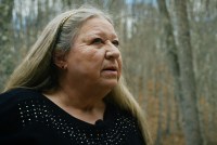 A woman wearing a black sweater poses for a portrait among tall trees
